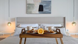 Un llit ben arrenjat amb una bandeja de menjar per esmorzar, incloent croissants, rodanxes de taronja i tasses de cafè, en una habitació d'hotel moderna.