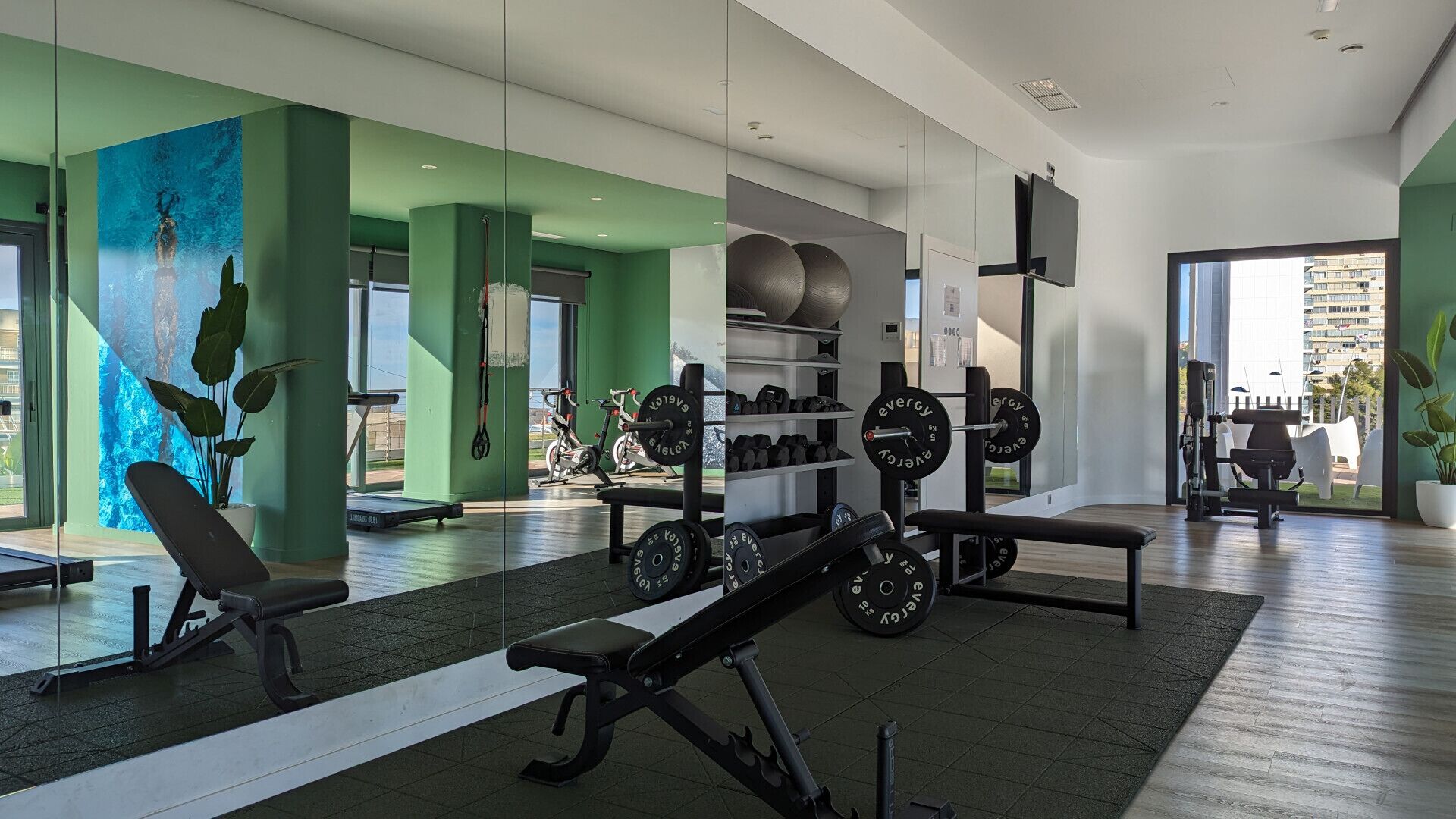 A modern gym with exercise equipment, a large mirror, and a view of the city.
