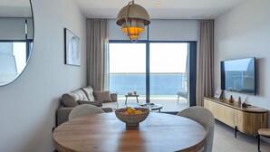 Un salon moderne avec une table ronde en bois, un canapé, un téléviseur et un balcon offrant une vue sur la mer.