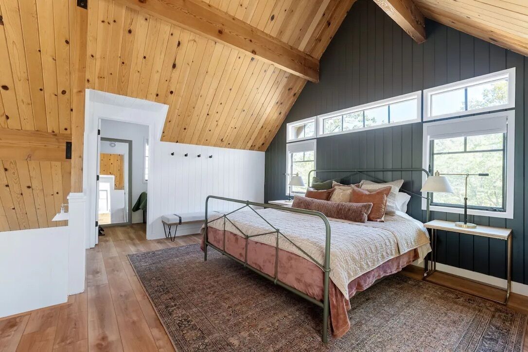 A bedroom with a sloped ceiling, a bed with a metal frame, a bedside table, and a window with multiple panes.