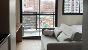 A modern bedroom with a large window, a sofa, and a view of the cityscape.