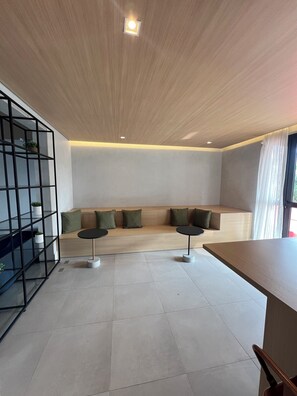 A modern living room with a wooden ceiling, a built-in seating area with cushions, and two small round tables.