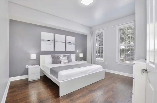 A modern bedroom with a large bed, two bedside tables, and a window with blinds.