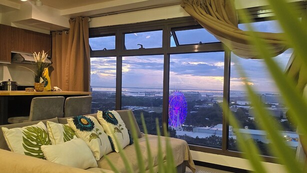 A modern bedroom with a large window, a sofa, a bed, and a view of a cityscape and a Ferris wheel. - 59sq/m Spacious and Safe condo+free parking+Manila Bay Sunset view/WiFi&NetFlx (Pasay)