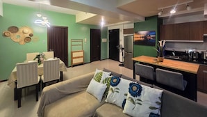 A modern living room with a sofa, dining table, and chairs. There is a kitchen area with cabinets and a refrigerator. - 59sq/m Spacious and Safe condo+free parking+Manila Bay Sunset view/WiFi&NetFlx (Pasay)