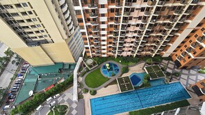 A high-rise residential building with multiple balconies, a swimming pool, and a landscaped courtyard. - 59sq/m Spacious and Safe condo+free parking+Manila Bay Sunset view/WiFi&NetFlx (Pasay)