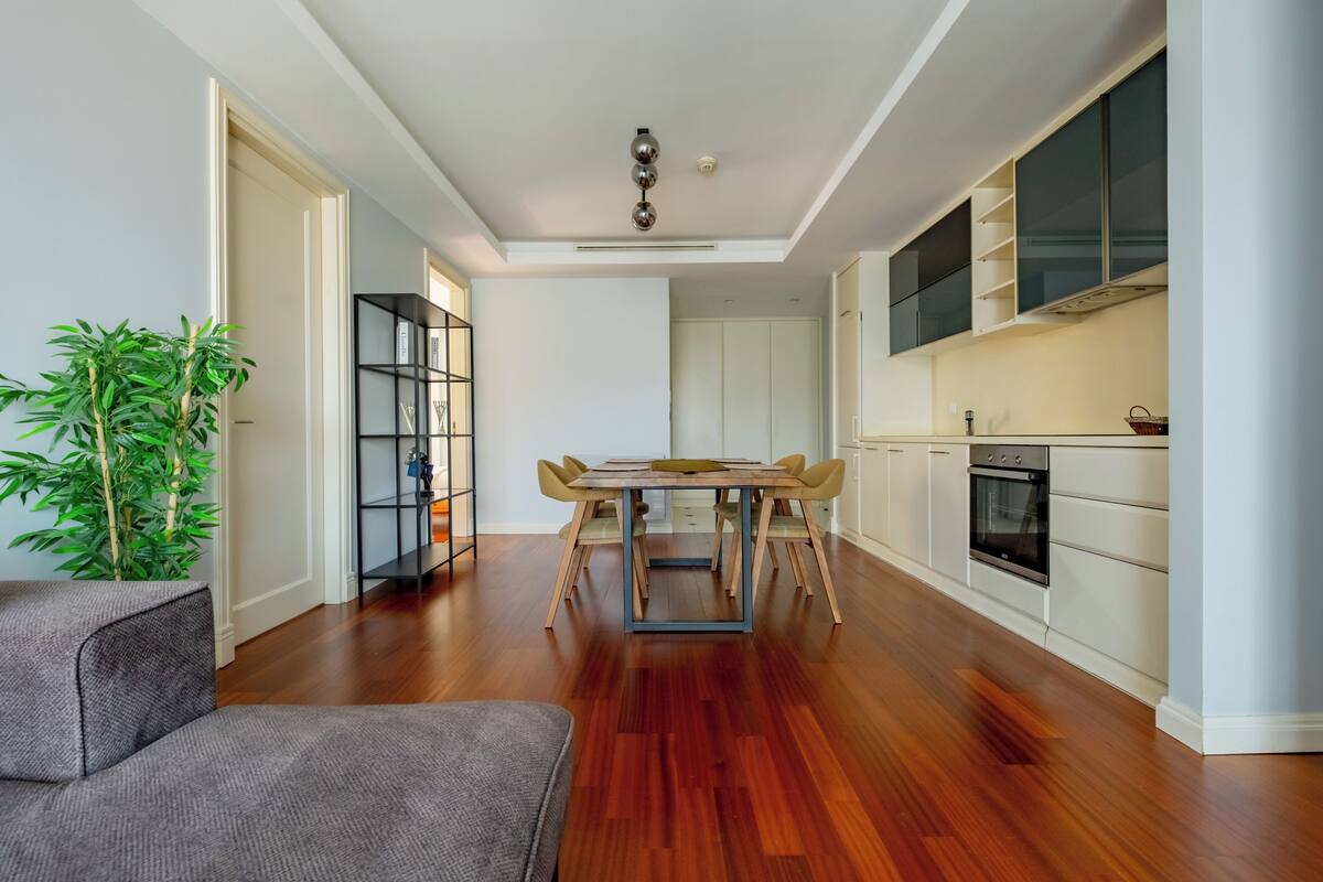 A modern kitchen with white cabinets, a dining area with a wooden table, and a large plant.