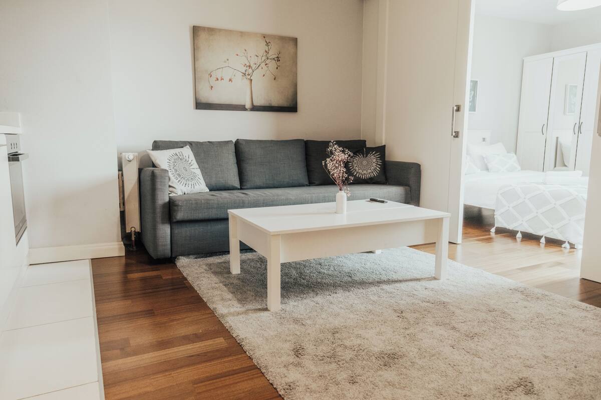 A modern living room with a grey sofa, white coffee table, and a painting on the wall.
