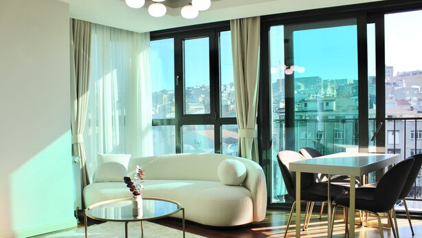 Un salon moderne avec un canapé, une table à manger et des chaises. De grandes fenêtres offrent une vue sur la ville.