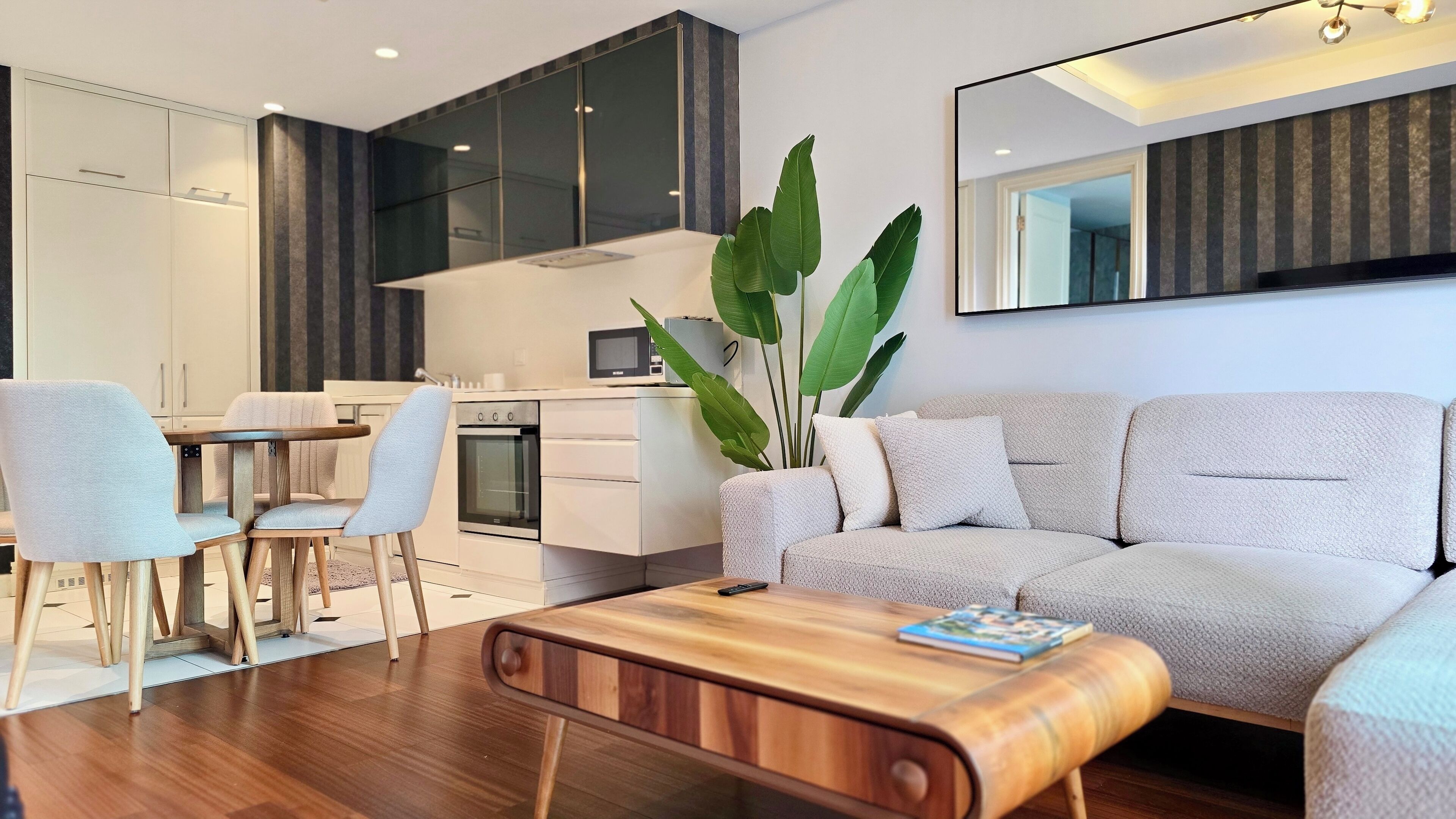 Un salon moderne avec un canapé, une table basse et des fauteuils. Il y a également un coin cuisine avec des placards et des appareils électroménagers.
