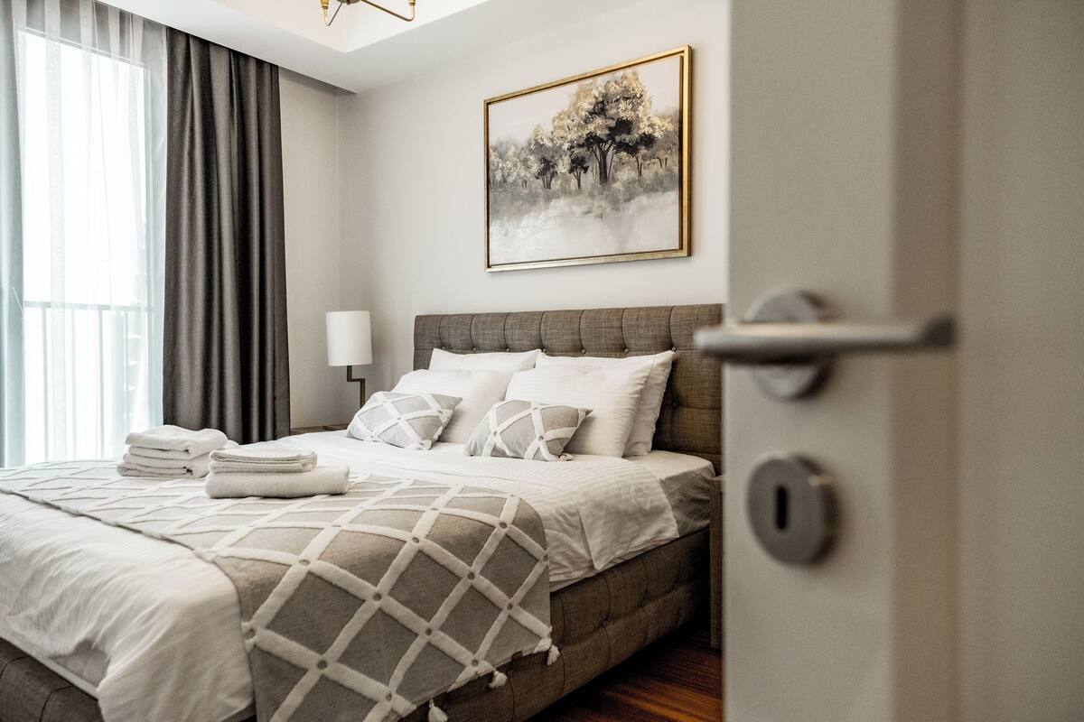 A neatly made bed with a geometric-patterned blanket, a bedside lamp, and a framed artwork on the wall.
