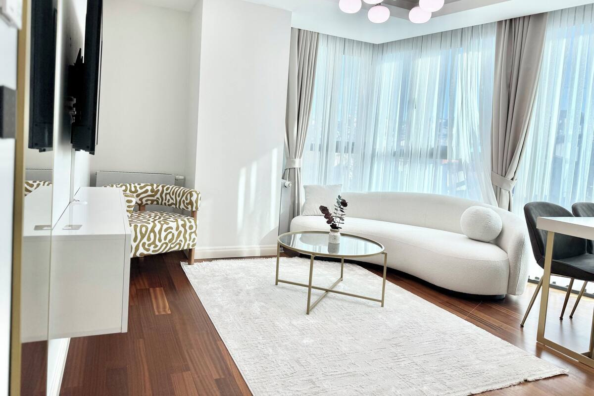 A modern living room with a sofa, a coffee table, a TV, and a view of the city through large windows.