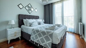 Une chambre à coucher moderne avec un grand lit, une table de chevet, une lampe et une fenêtre avec des rideaux.