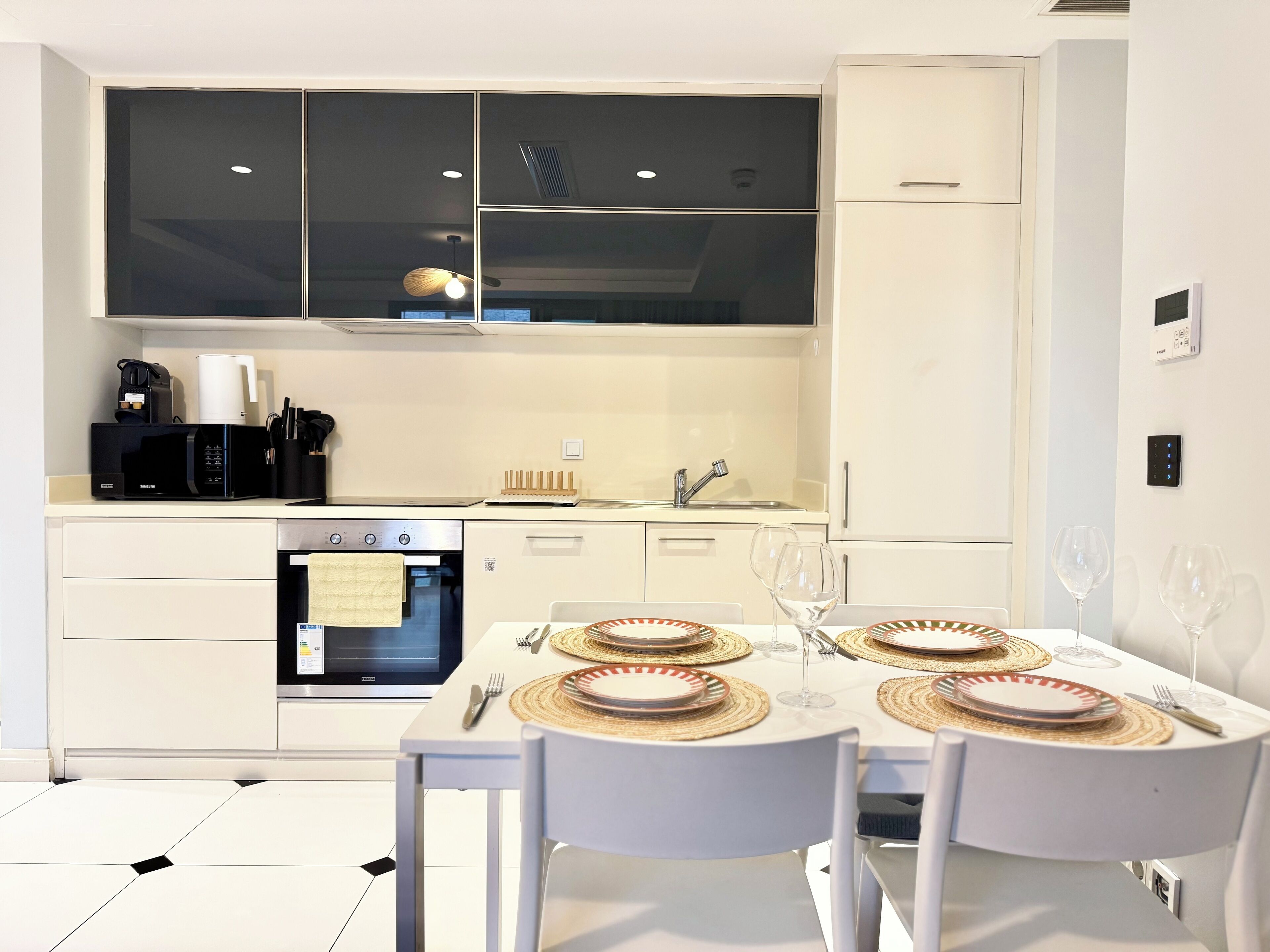A modern kitchen with white cabinetry, a built-in oven, and a dining area set for four with a white table and chairs.