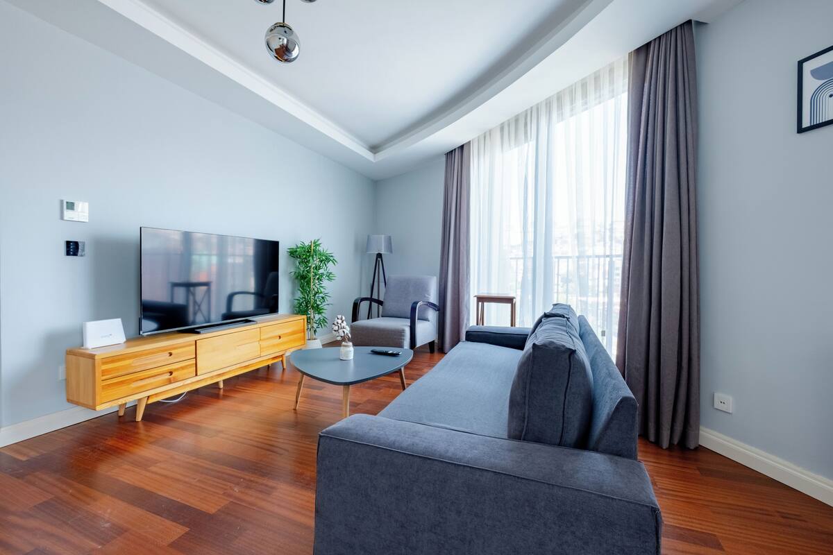 A modern living room with a grey sofa, wooden TV stand, and a large flat-screen TV.