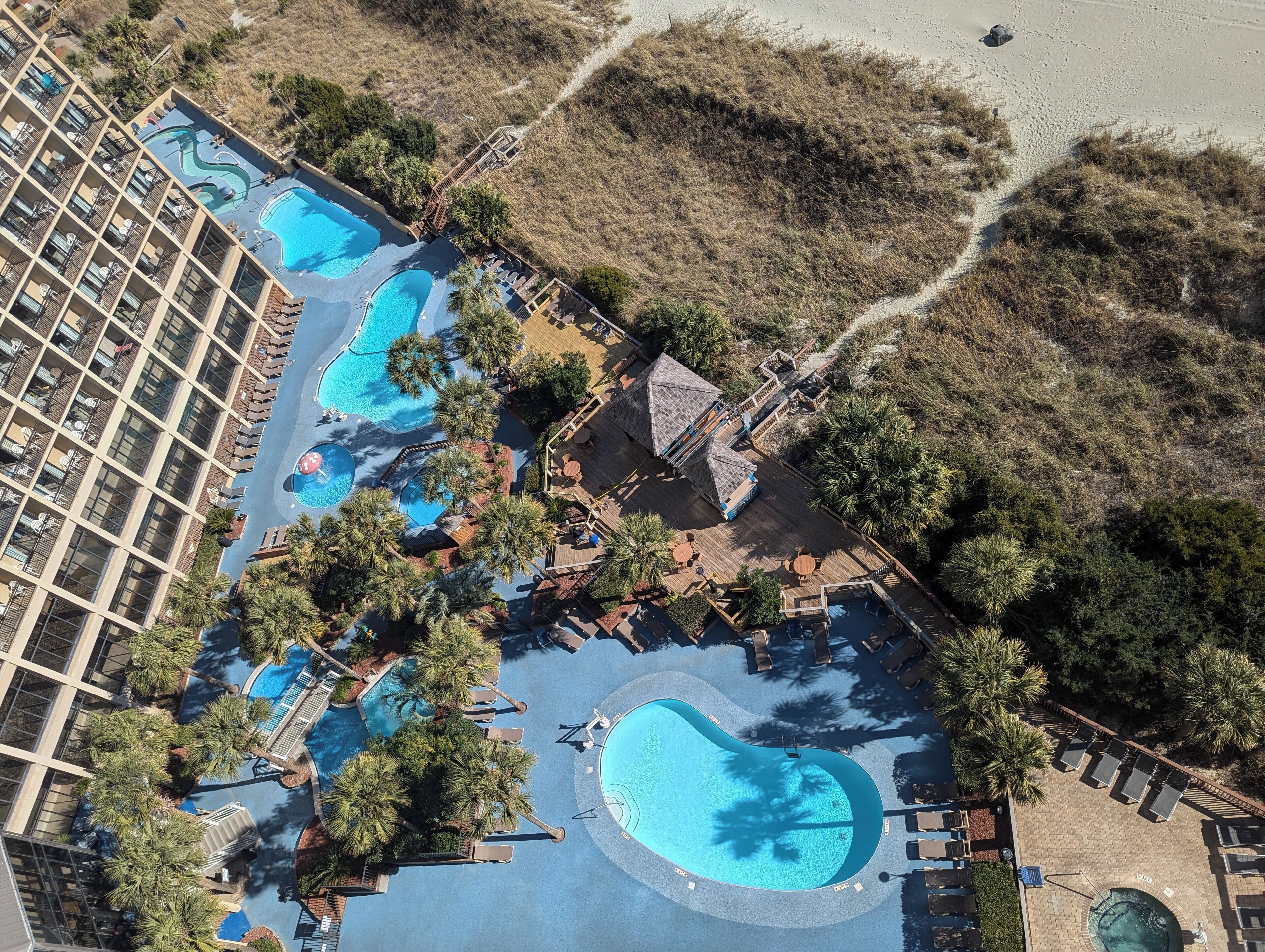 An aerial view of a resort with multiple swimming pools, palm trees, and a large building with balconies.