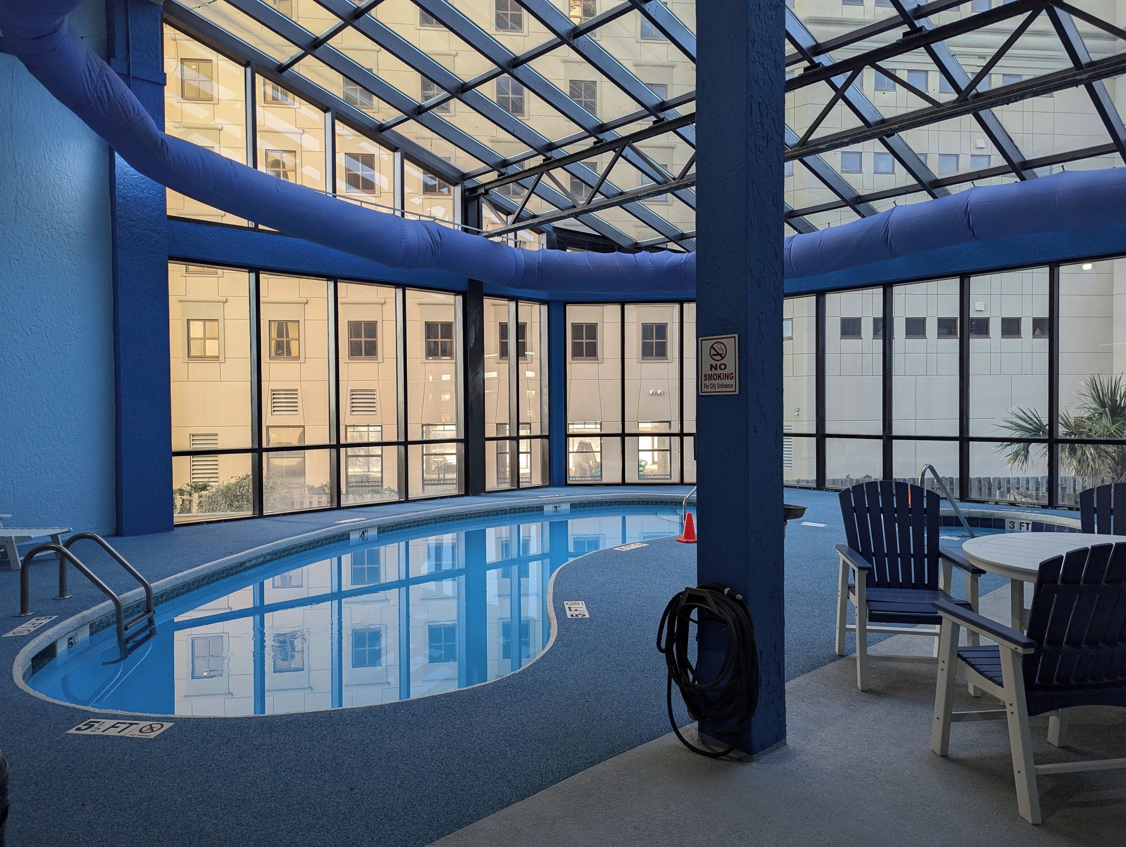 Une piscine intérieure avec des parois en verre transparent, un sol bleu et un panneau indiquant qu'il est interdit de fumer.