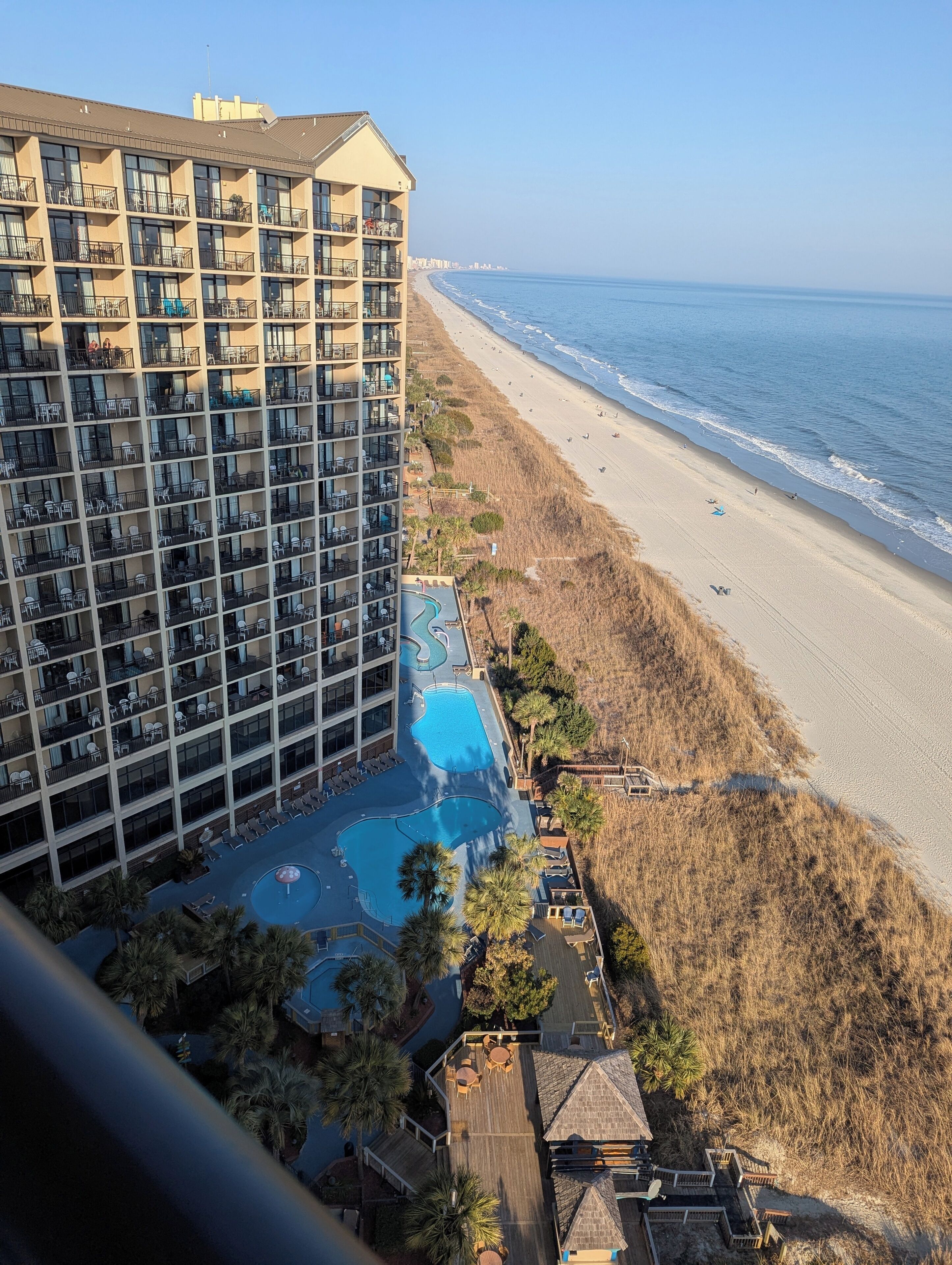 Un hotel de gran altura con varios balcones, una piscina y vista a la playa.