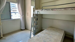 A compact room with a bunk bed, a ladder, a ceiling fan, and a window with curtains. - SEASIDE APARTMENT IN GUILHERMINA (Guilhermina Praia Grande)