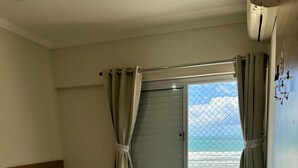A bedroom with a bed, a window with curtains, a ceiling fan, and a view of the beach. - SEASIDE APARTMENT IN GUILHERMINA (Guilhermina Praia Grande)