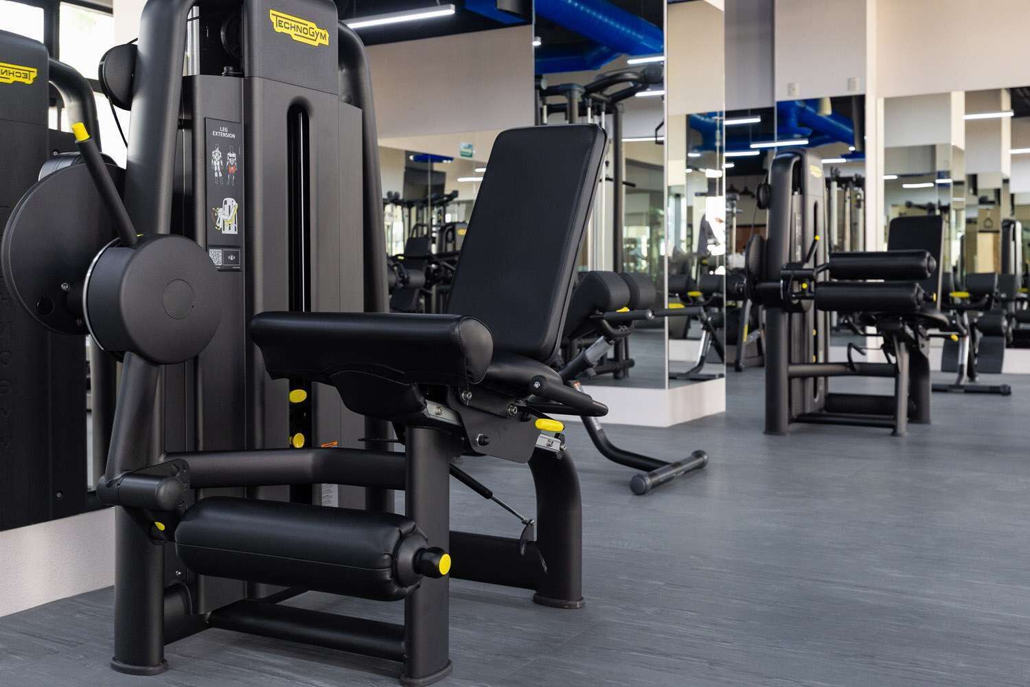 Ett gym med olika träningsmaskiner, inklusive maskiner för bensträck och bröstpress.