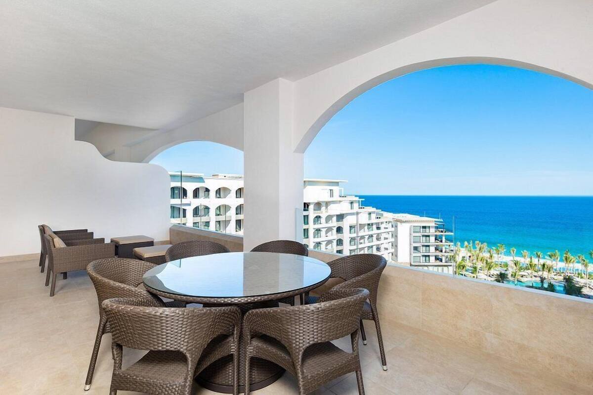 Ein runder Tisch mit Korbstühlen auf einem Balkon mit Blick auf das Meer und ein Resort.