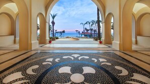 A corridor with a patterned floor leading to a beach view, palm trees, and a sunset. - Villa la Valencia  (San José del Cabo)