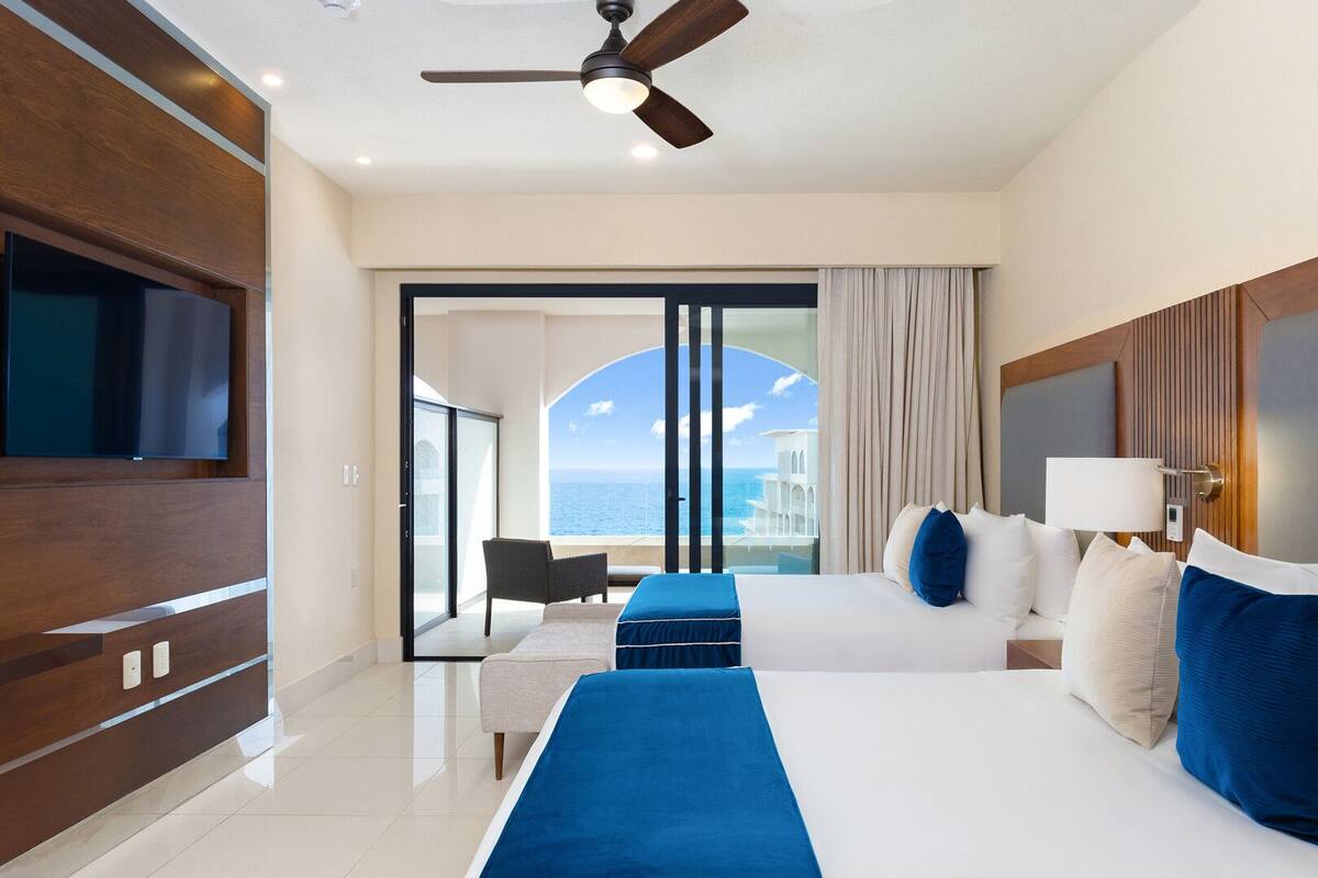 Ein Hotelzimmer mit einem großen Bett, einem Fernseher, einem Deckenventilator und Meerblick.