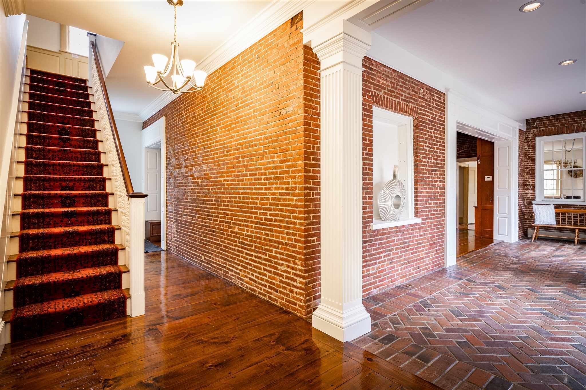 A spacious hallway with a brick wall, a wooden staircase, and a herringbone-patterned floor.