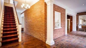 A spacious hallway with a brick wall, a wooden staircase, and a herringbone-patterned floor.