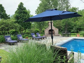 A poolside area with lounge chairs, a stone fireplace, and a pool.