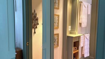 Un couloir doté d’un plancher en bois, d’une porte bleue et d’une salle de bain équipée d’un porte-serviettes et d’étagères.
