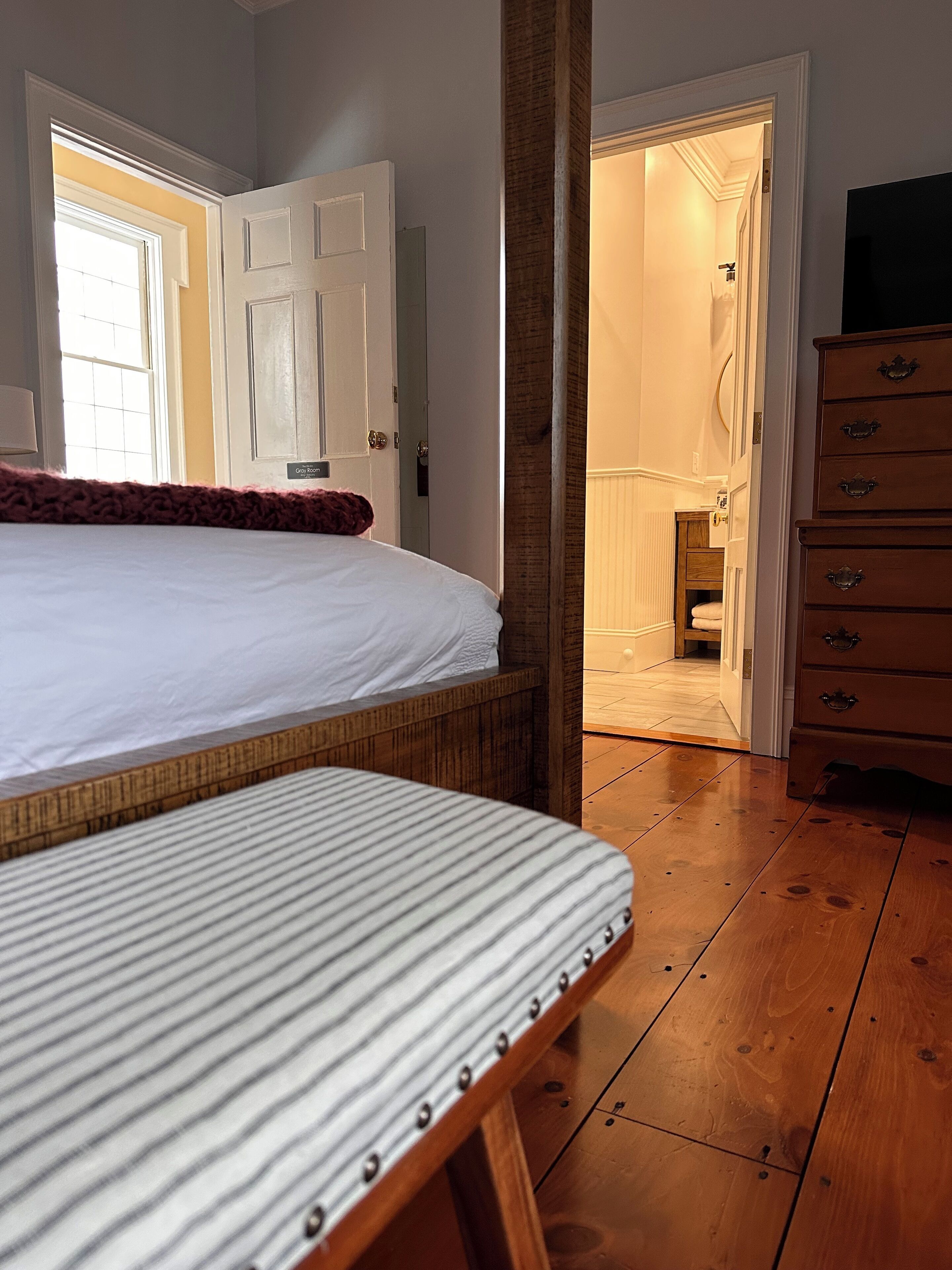 A bedroom with a bed, a wooden dresser, and a door leading to a bathroom.