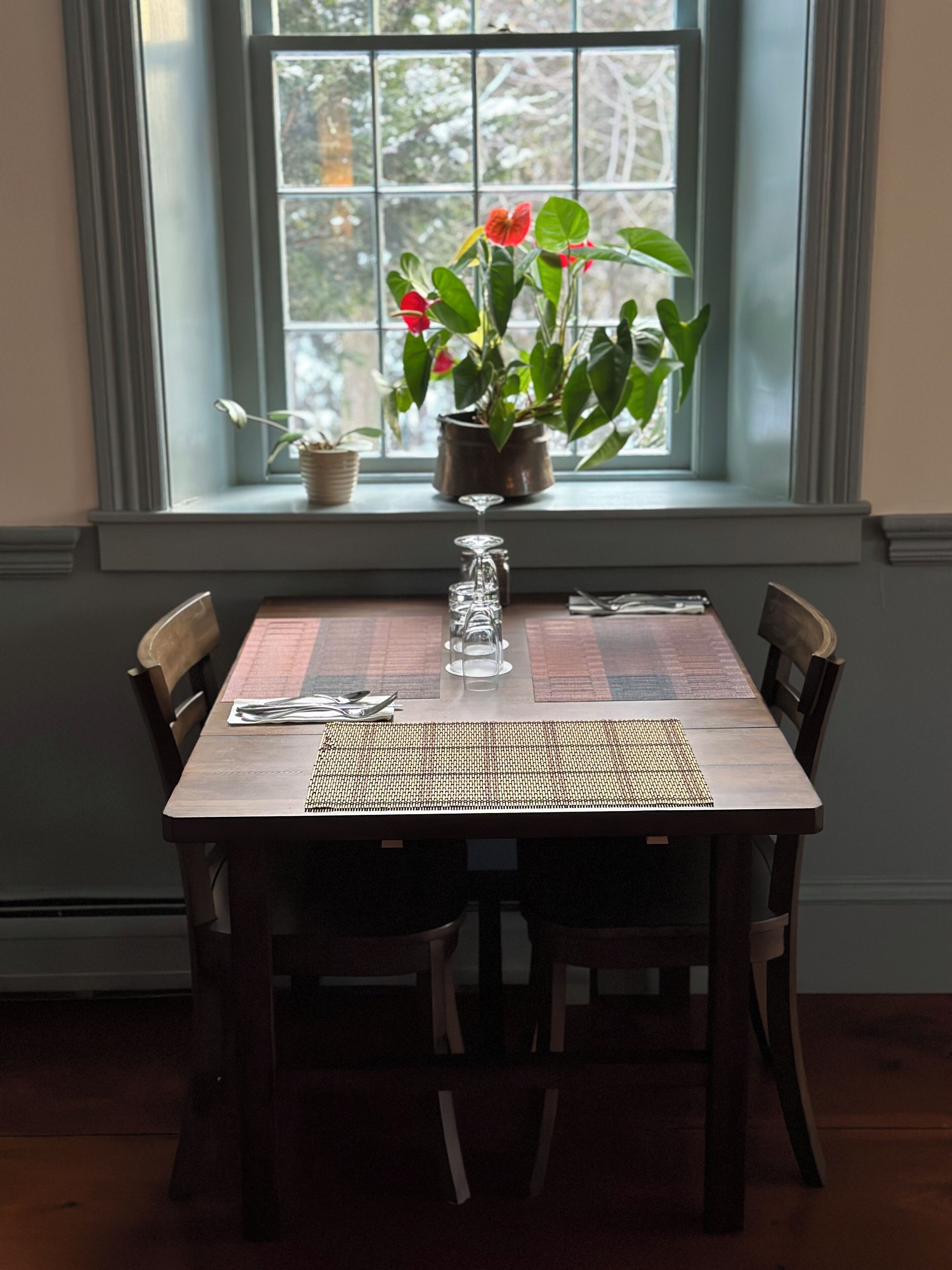 A dining table set for two with a placemat, a glass, and a potted plant with red flowers.
