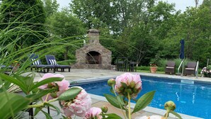 En swimmingpool med pionblommor i förgrunden, solstolar och en steneldstad i bakgrunden.