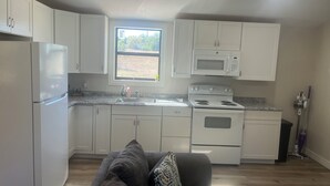 Una cucina compatta con mobili bianchi, un frigorifero, un forno a microonde, un fornello e una finestra vista verde.
