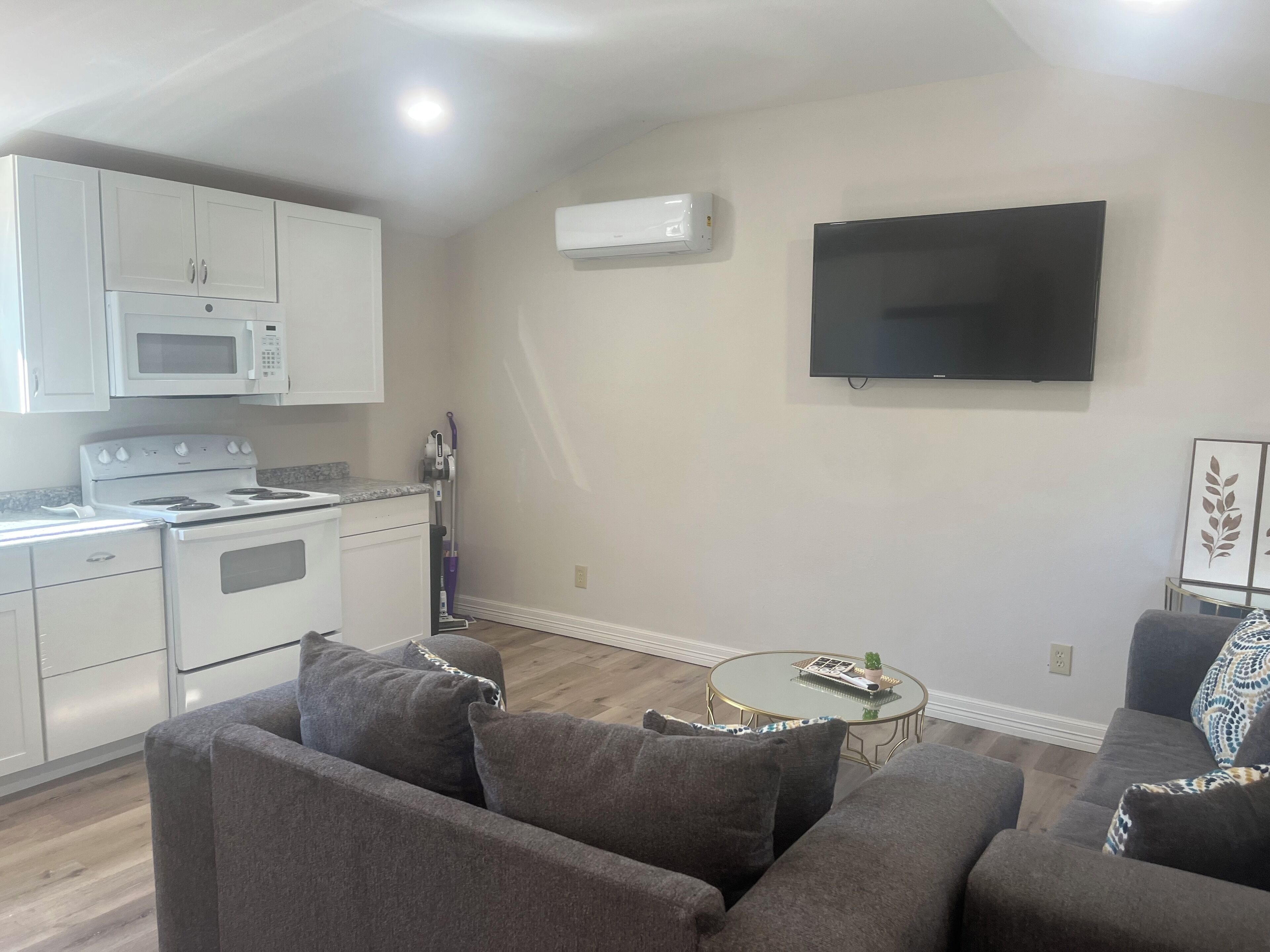 A modern living room with a grey sofa, a small round coffee table, and a flat-screen TV mounted on the wall.