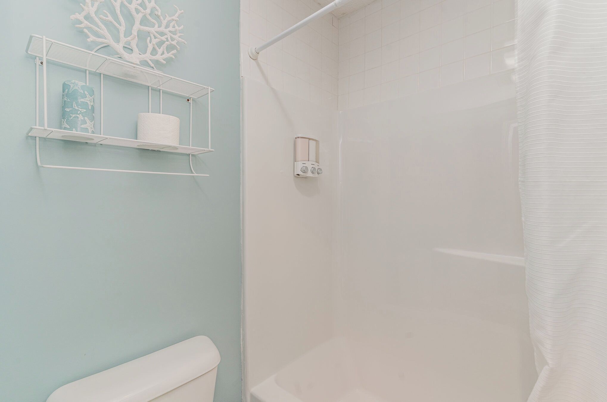 Un baño con ducha, inodoro y estante con rollo de papel higiénico y un objeto decorativo.