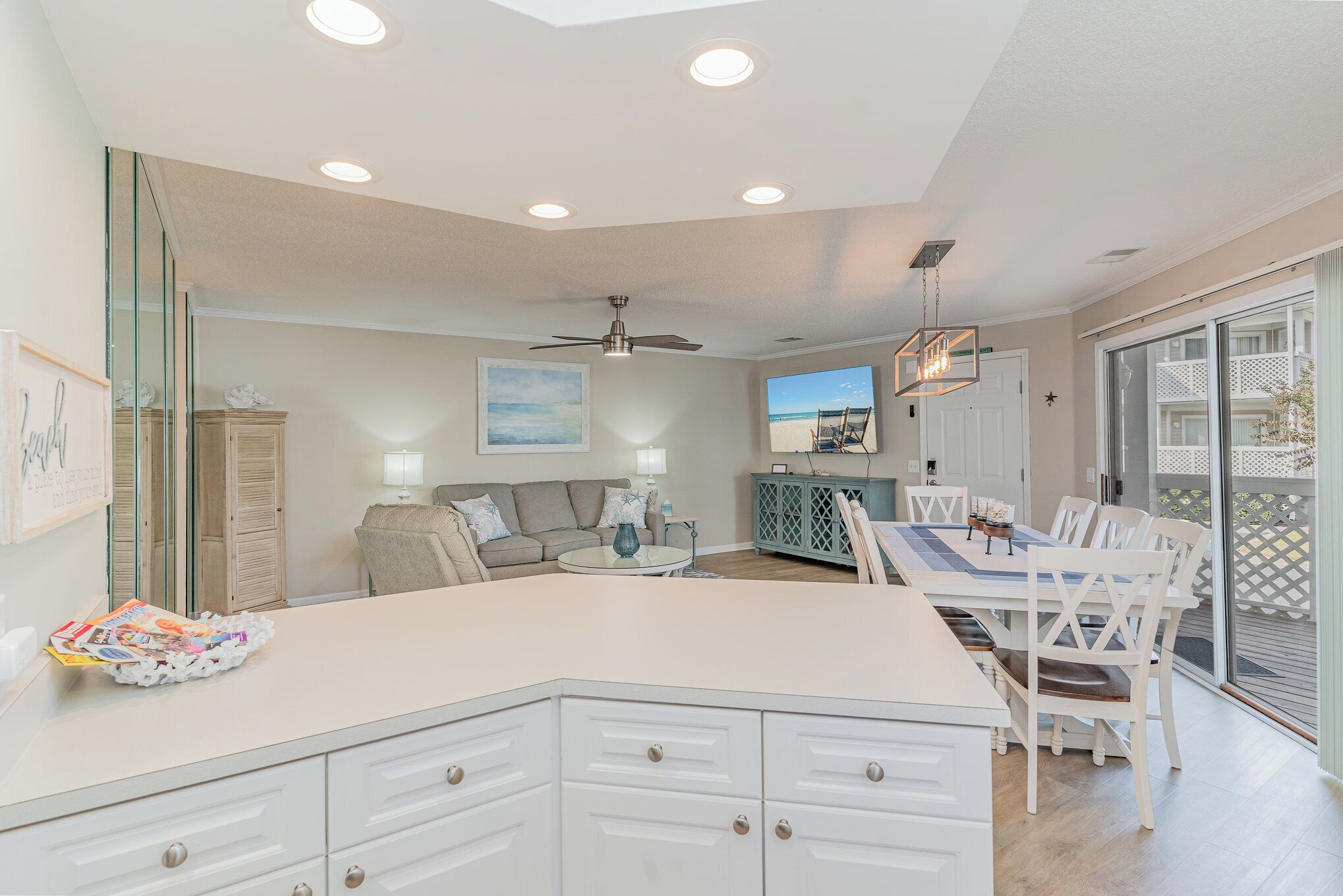 A modern kitchen with a central island, a dining area with white chairs, and a view of the outdoors through large sliding glass doors.