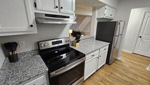 A kitchen with white cabinets, a black stove, a granite countertop, and a refrigerator. - N. Columbus Townhome with 3bd, 2.5ba, Centrally Located! (Columbus)