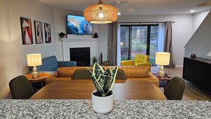 A modern living room with a fireplace, a dining table with chairs, and a large window with curtains. - N. Columbus Townhome with 3bd, 2.5ba, Centrally Located! (Columbus)