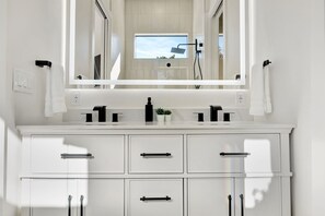 A modern bathroom with a large mirror, two sinks, a potted plant, and a window. - New Upscale Retreat Downtown Dunedin w/ Balcony! Sleeps 4 (Dunedin)