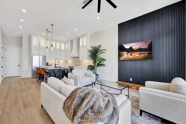 A modern living room with a sofa, a coffee table, and a dining area with chairs and a table. - New Upscale Retreat Downtown Dunedin w/ Balcony! Sleeps 4 (Dunedin)