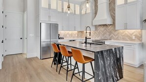 A modern kitchen with white cabinetry, a marble island, and orange bar stools.