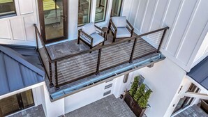 A balcony with two chairs and a table, a railing, and a view of the street below.