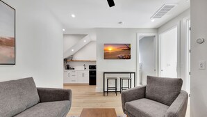 A modern living room with two grey sofas, a wooden coffee table, and a kitchen in the background.