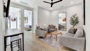 A modern living room with a sofa, armchairs, a coffee table, and a TV mounted on the wall.