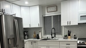 A modern kitchen with white cabinetry, a stainless steel refrigerator, a large island with stools, and a window with blinds. - 2-bedroom with private pool in Fort Myers Beach 2 minute walk to beach (Fort Myers Beach)