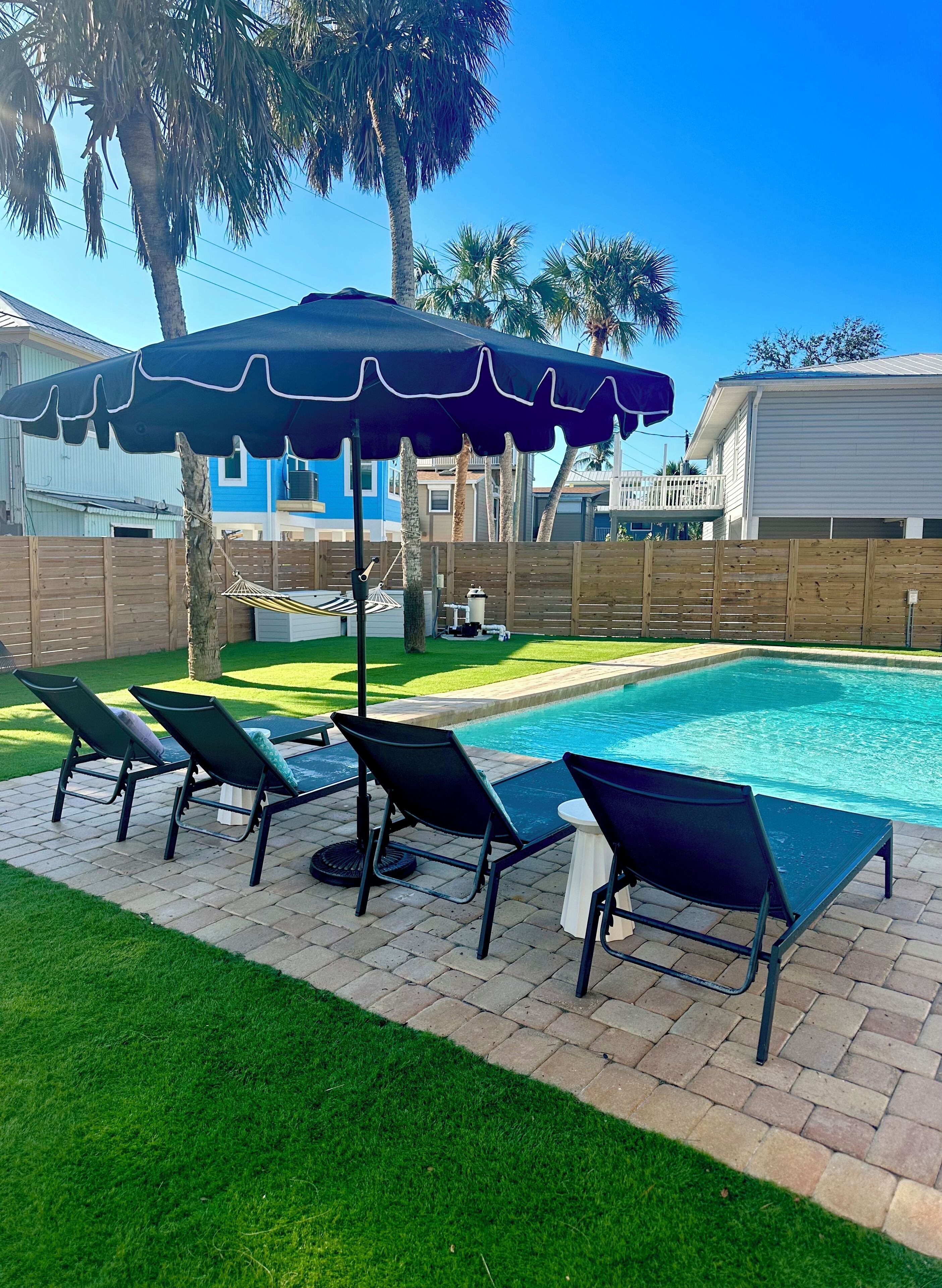 A backyard with a swimming pool, four lounge chairs, a table, and a blue umbrella.