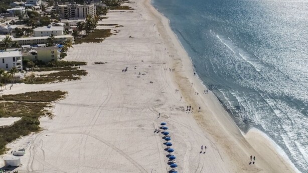 A beach with a row of blue umbrellas, a sandy shore, and buildings in the background. - 2-bedroom with private pool in Fort Myers Beach 2 minute walk to beach (Fort Myers Beach)